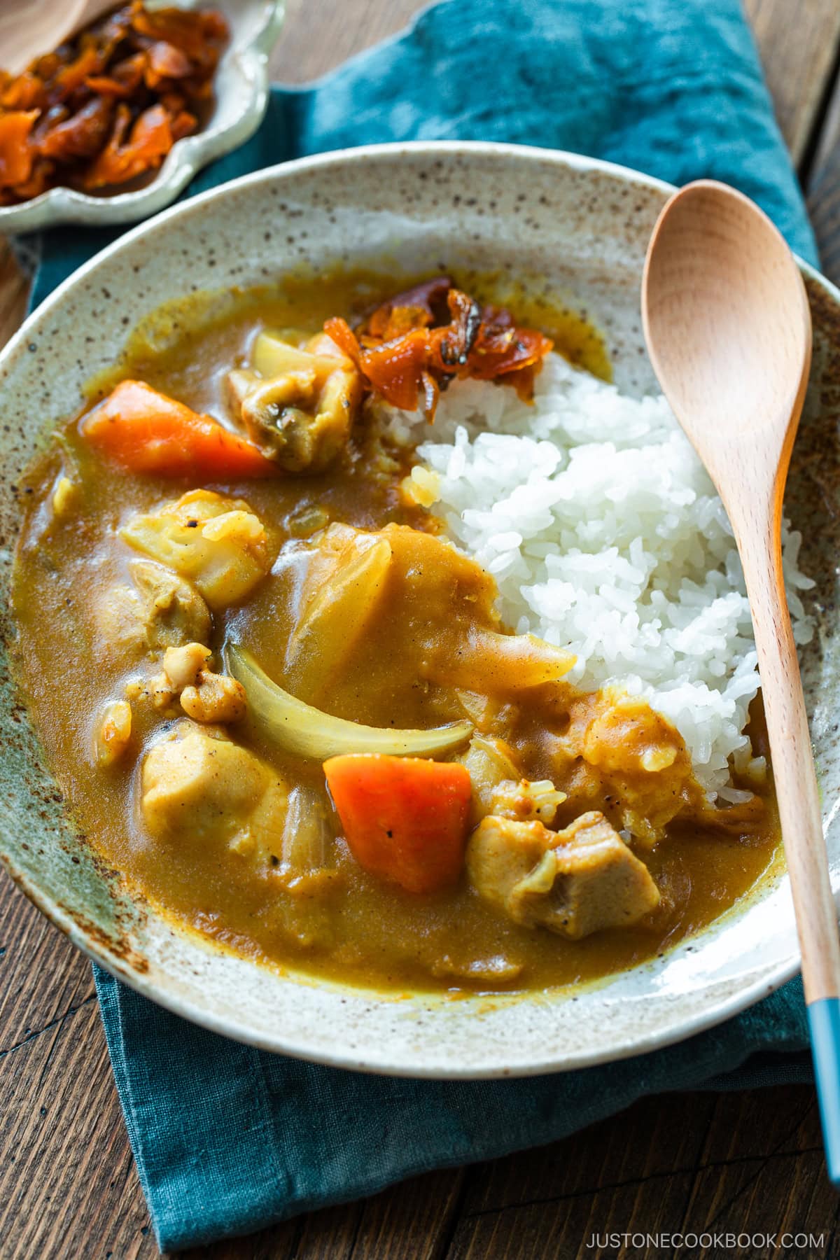 A round plate containing Japanese chicken curry over steamed rice, garnished with fukujinzuke pickles.