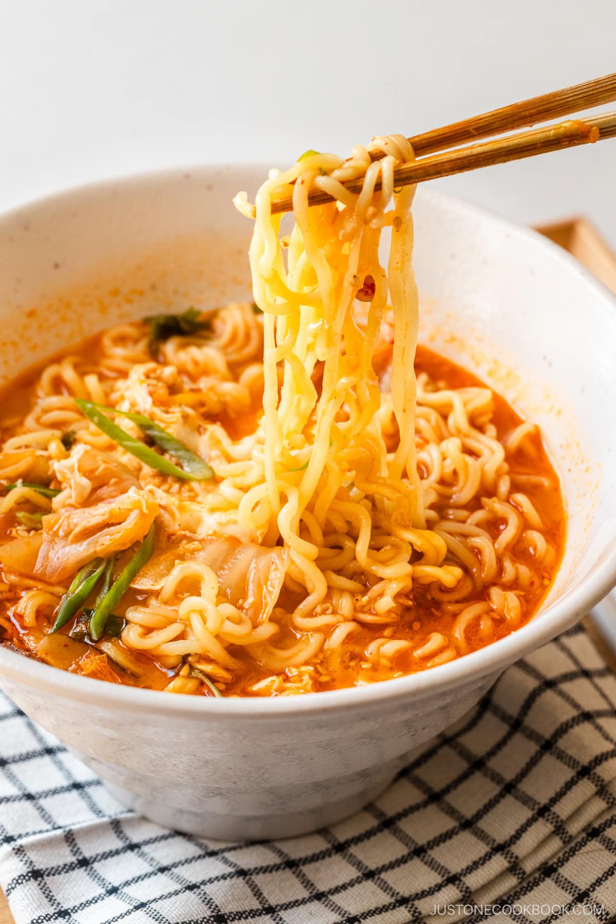 A white ramen bowl containing Korean ramen (ramyeon), topped with soft-cooked egg, kimchi, and green onions.