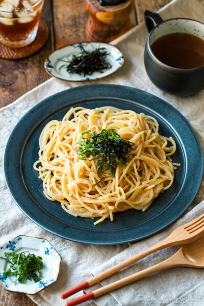 A black round plate containing metaiko pasta - Japanese spaghetti with spicy salted cod roe topped with julienned shiso and shredded nori seaweed.