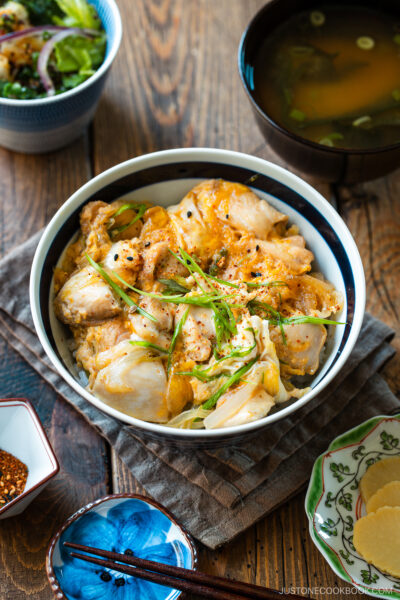 A Japanese ceramic bowl containing Oyakodon, a chicken and egg rice bowl dish garnish with green onion.