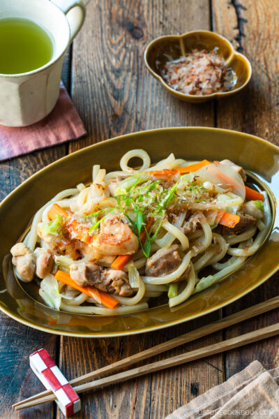 An olive colored oval plate containing Yaki Udon, Japanese stir-fried udon noodles with chicken and vegetables.