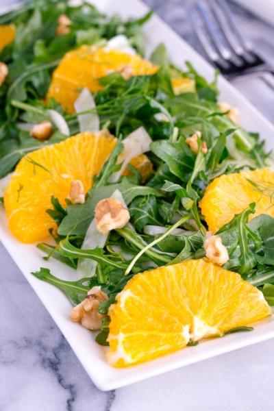 A white rectangular plate containing arugula salad with fennel and navel orange.