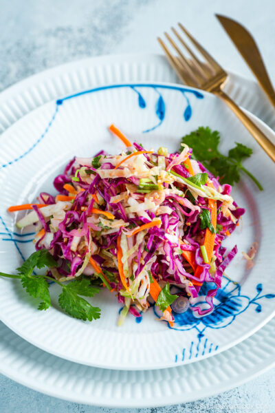 Asian Coleslaw with Sesame Dressing on a white plate along with gold fork and knife.