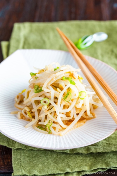 A white plate containing Bean Sprout Salad, seasoned with sesame oil and mixed with (ground) sesame seeds and green onions.