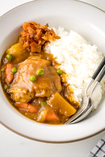 A white ceramic bowl containing steamed rice and Japanese bone-in chicken curry garnished with fukujinzuke.