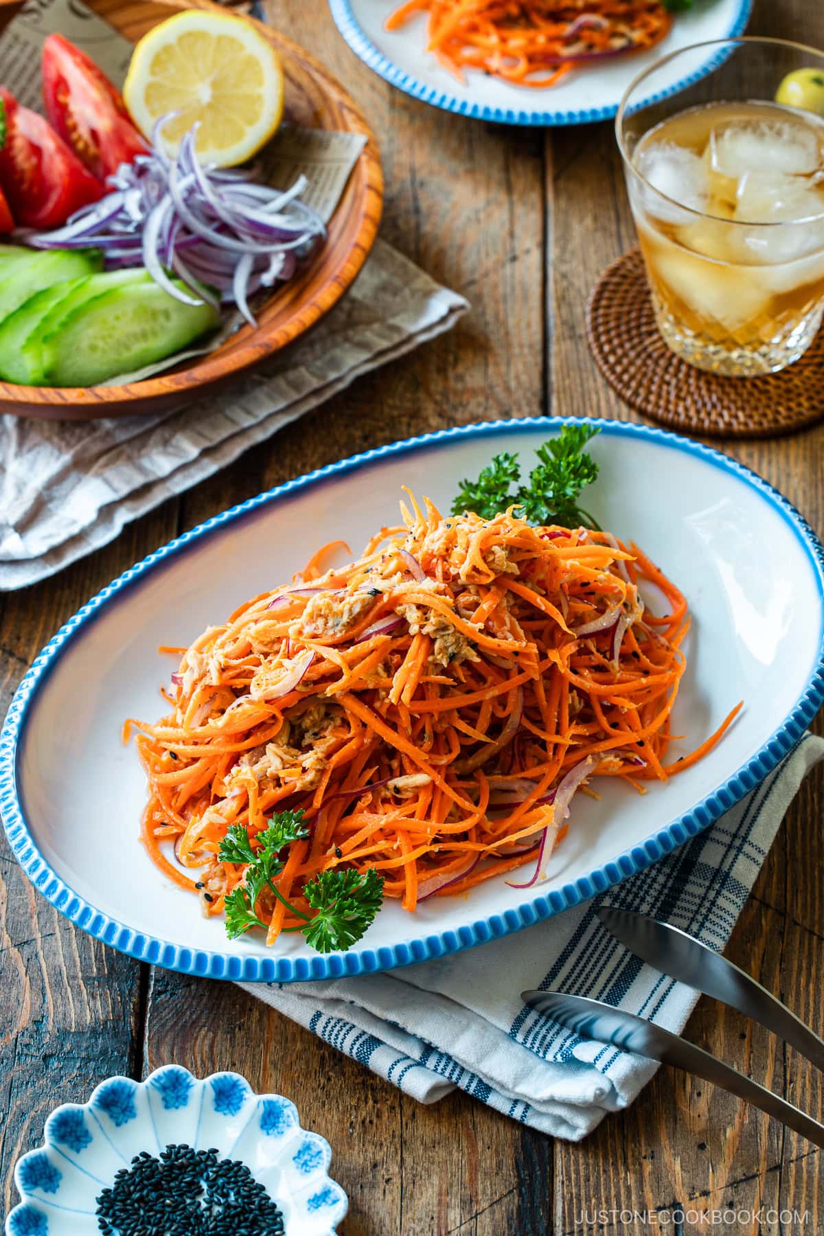 An oval scalloped plate containing shredded carrot and tuna salad garnished with parsley and lemon.