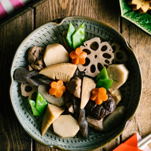 A Japanese ceramic bowl containing simmered chicken and vegetables.