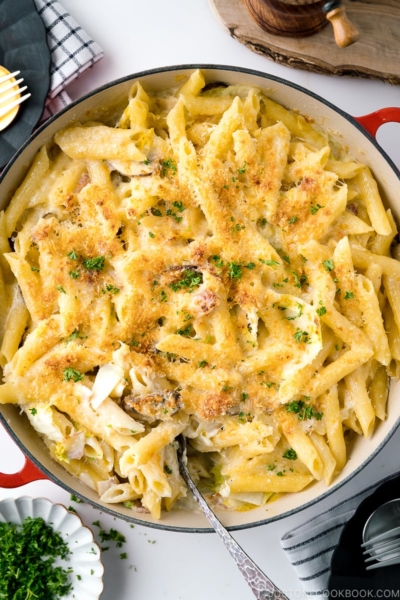 A red Le Creuset braiser containing creamy napa cabbage and bacon pasta.