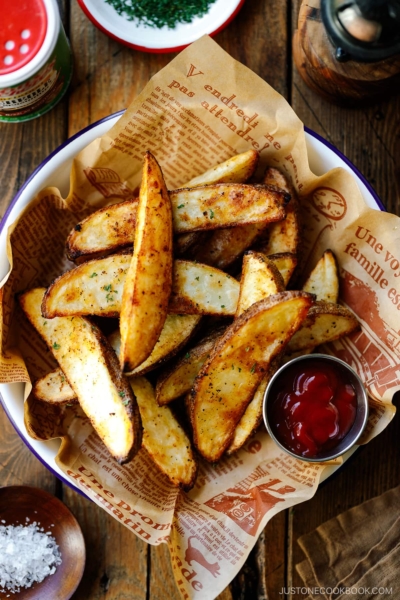 A white and blue enamel bowl containing Crispy Baked Potato Wedges with ketchu in a mini container.