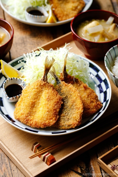 A plate containing panko-coated, fried horse mackerel fillets and a bed of shredded cabbage salad.