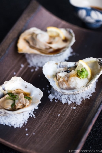 Dark Japanese plate containing Grilled Oysters with 3 kinds of garnish and Ponzu Sauce