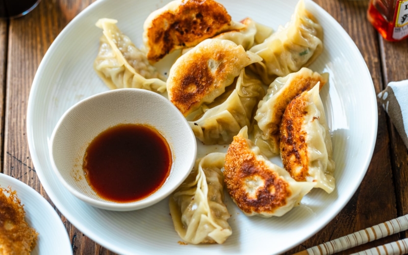 A round plate containing gyoza (Japanese potstickers or pan-fried dumplings) with a small plate of dipping sauce made with soy sauce, vinegar, and Japanese chili oil.