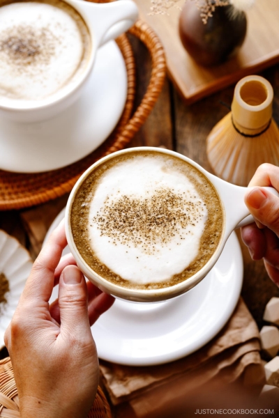 White cups containing Hojicha Latte topped with roasted green tea powder.