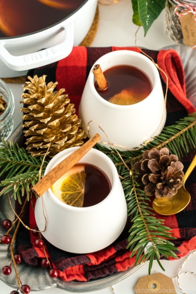 White cups containing hot mulled cider garnished with orange slice and a cinnamon stick.