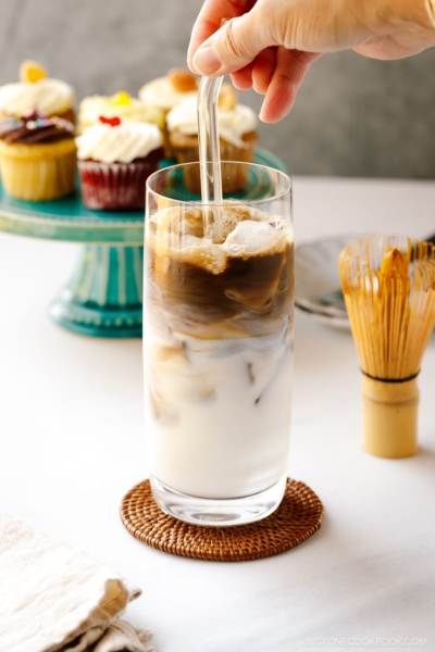 A tall glass filled with iced hojicha latte, showing two layers of milk and chocolate-color roasted green tea (hojicha).