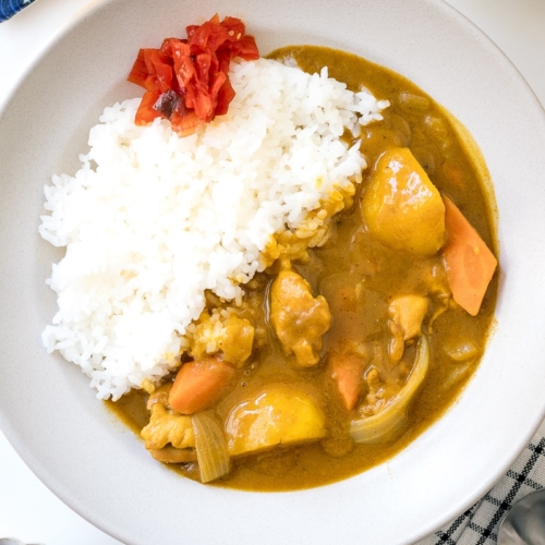 A ceramic bowl containing Japanese Chicken Curry along with steamed rice and fukujinzuke pickles.