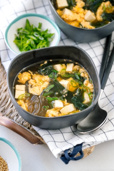 Black ceramic bowls containing glass noodle soup with tofu, fluffy egg, and wakame seaweed.