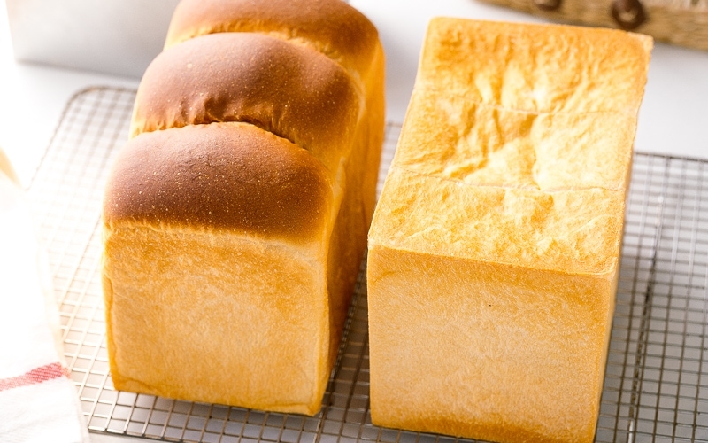 Two loaves of Japanese milk bread (flat-topped and round-topped) on a wire rack.