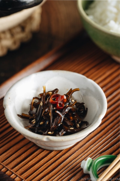 Simmered kombu in a small dish next to a bowl of steamed rice.