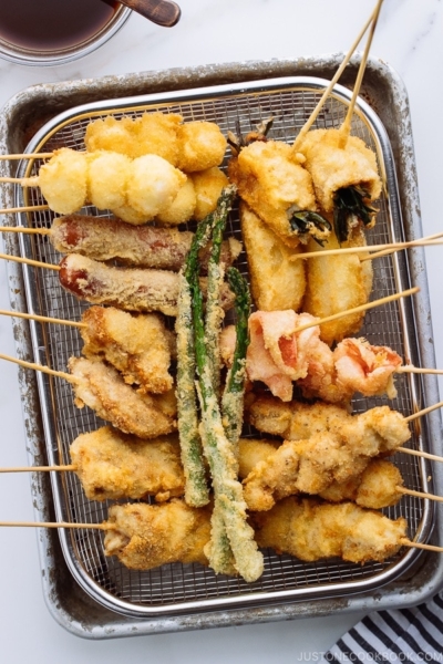 Wire basket containing golden and crispy Kushikatsu (Kushiage) served with savory sauce.