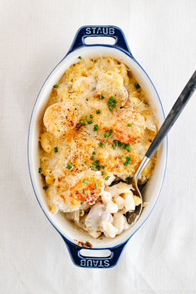 A spoon scooping out creamy macaroni gratin served in a blue STAUB gratin dish.