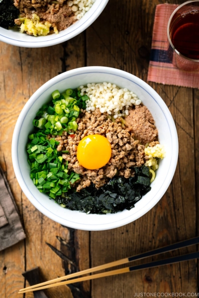 A bowl containing Mazesoba (Mazemen), Japanese Brothless Ramen, topped with seasoned minced meat, green onion, garlic chives, nori seaweed, crushed garlic, and katsuobushi powder.