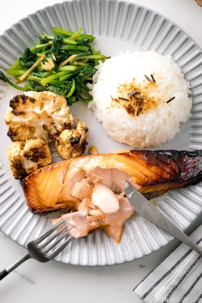 A ceramic plate containing Mirin Salmon along with steamed rice, roasted cauliflower, and sauteed greens.