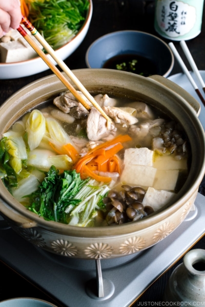 A Japanese earthenware pot (donabe) containing Mizutaki (Japanese Chicken Hot Pot) filled with chicken, tofu, mushrooms, and all kinds of vegetables.