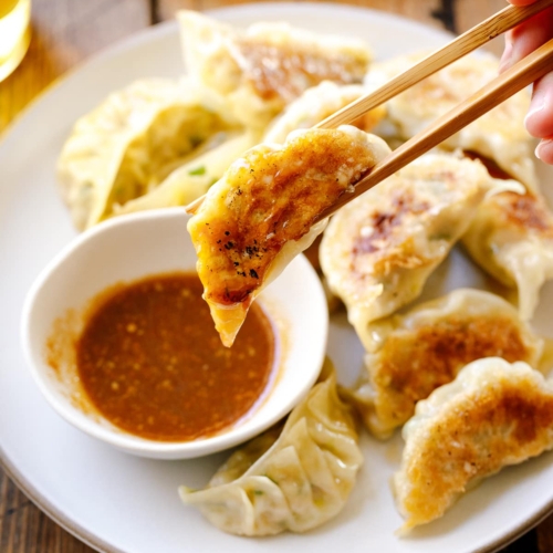 A round plate containing Japanese pan-fried dumplings, Napa Cabbage Gyoza, served with a savory miso dumpling sauce.