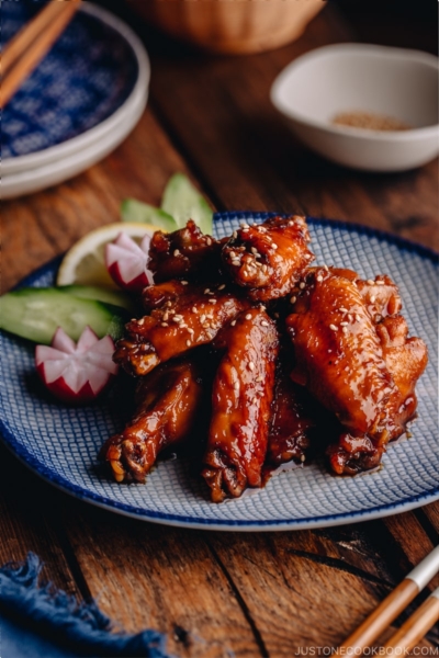 Orange teriyaki chicken wings on a blue patter.