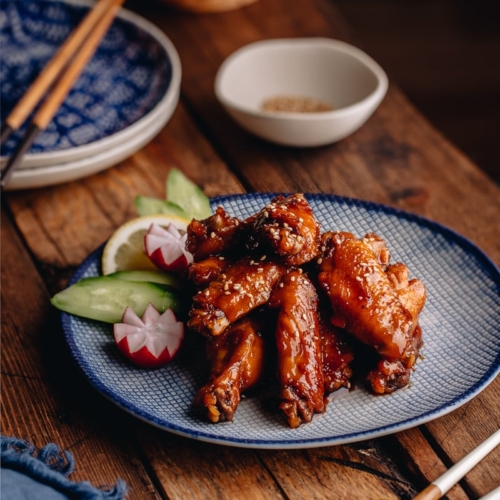 Orange teriyaki chicken wings on a blue patter.