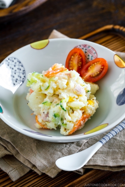 A ceramic bowl containing Japanese potato salad and cherry tomatoes.