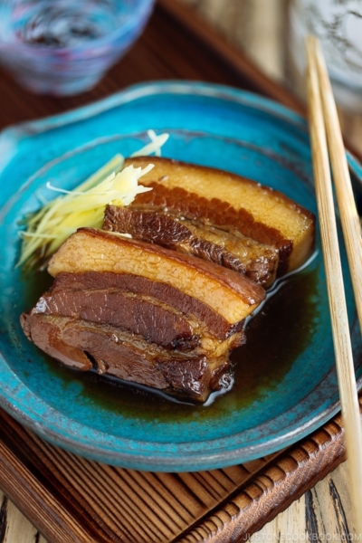 A blue plate containing 2 slices of Rafute (Okinawan Braised Pork Belly) garnished with julienned ginger.