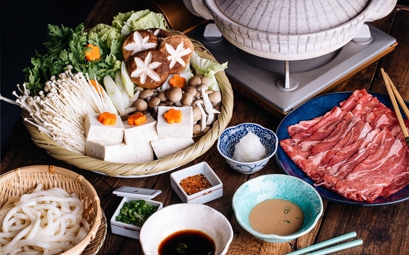 Tablesetup for shabu shabu - donabe hot pot, vegetables, meat, udon, and dipping sauces.