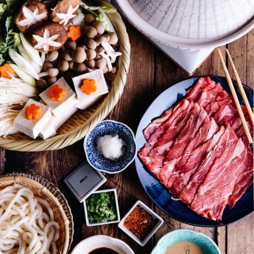 Tablesetup for shabu shabu - donabe hot pot, vegetables, meat, udon, and dipping sauces.