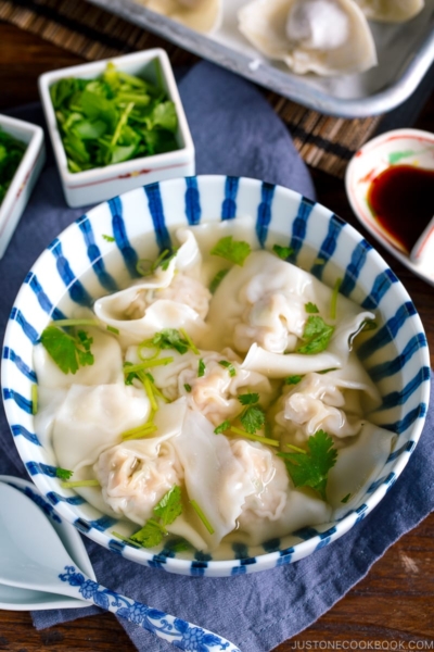 a large bowl containing shrimp and wonton soup along with the condiments.