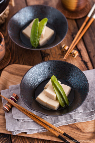 Simmered koyadofu with snow peas in a black ceramic bowl.