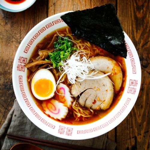 Ramen bowls containing Spicy Shoyu Ramen topped with chashu, marinated egg (ajitama), fish cake, scallions, and nori.