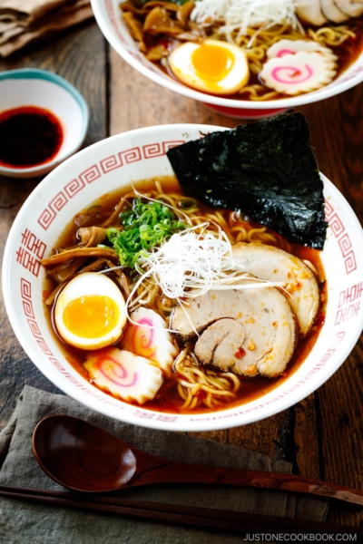 Ramen bowls containing Spicy Shoyu Ramen topped with chashu, marinated egg (ajitama), fish cake, scallions, and nori.