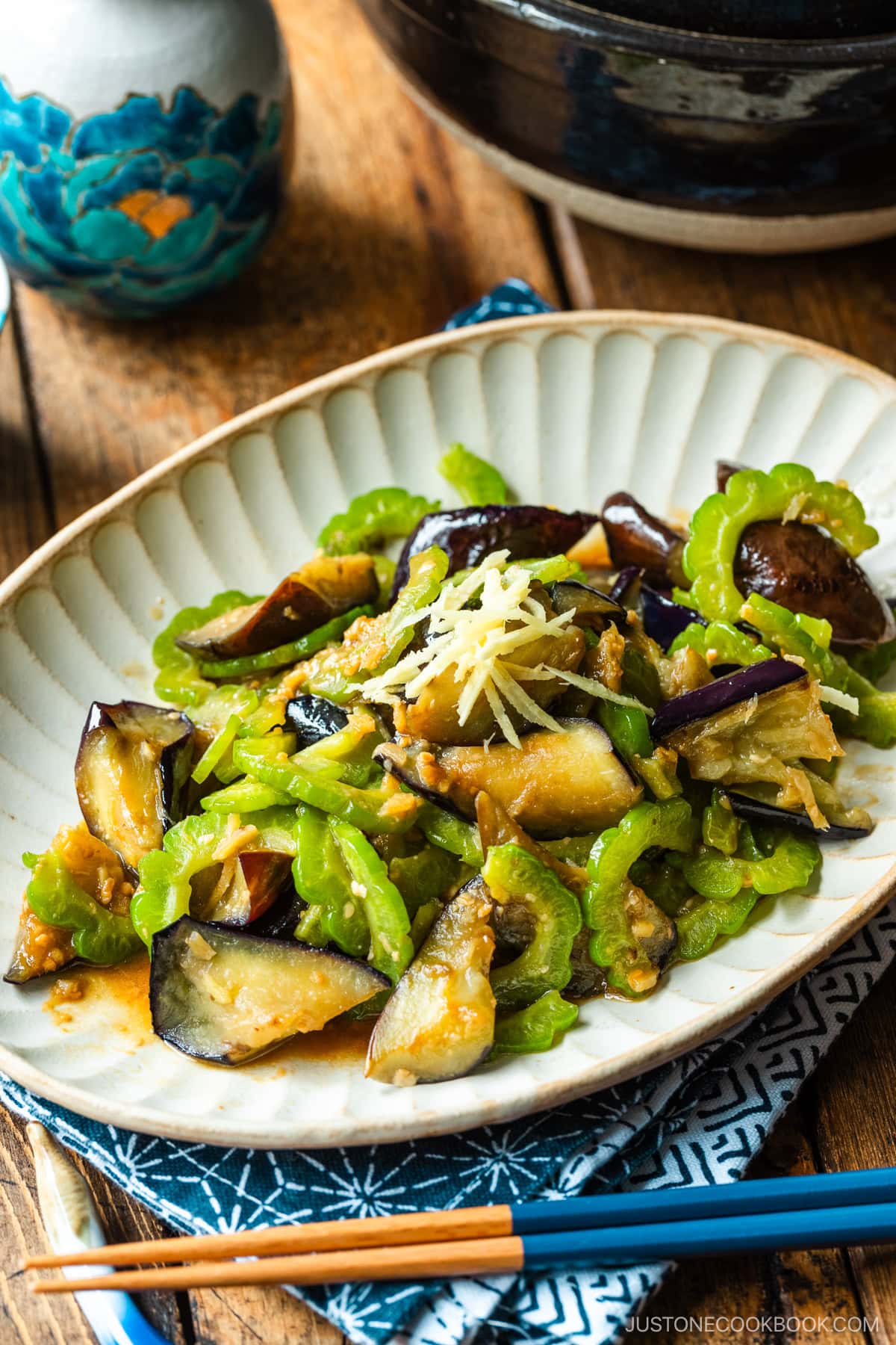 An oval fluted plate containing Stir-Fried Bitter Melon and Eggplant topped with julienned ginger.