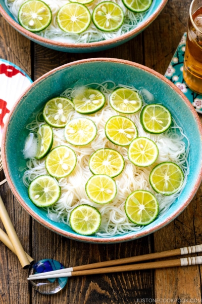 A blue bowl containing cold somen noodles topped with thinly sliced sudachi citrus.