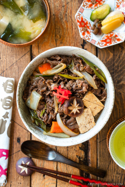 A large ceramic donburi rice bowl containing Sukiyaki Don, thinly sliced beef, tofu, and vegetables simmered in a savory dashi soy broth and served over steamed rice.