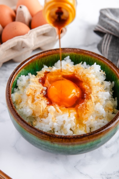 A bowl containing steamed rice, raw egg, sprinkled katsuobushi, and a drizzle of soy sauce.