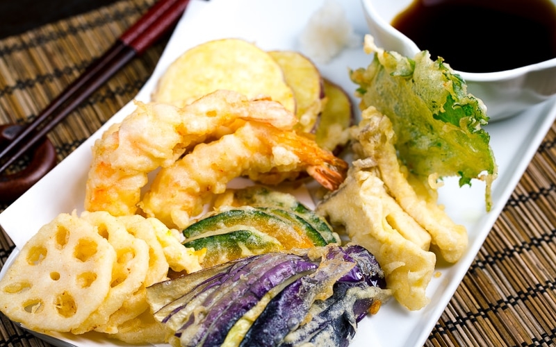 Shrimp and vegetable tempura on a plate along with the dipping sauce.