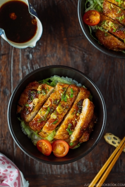 A black bowl containing Teriyaki Pork over steamed rice drizzled with homemade teriyaki glaze.