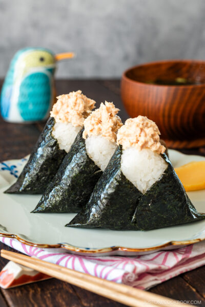 A plate containing three tuna mayo onigiri and pickles, served with a wooden bowl of miso soup.