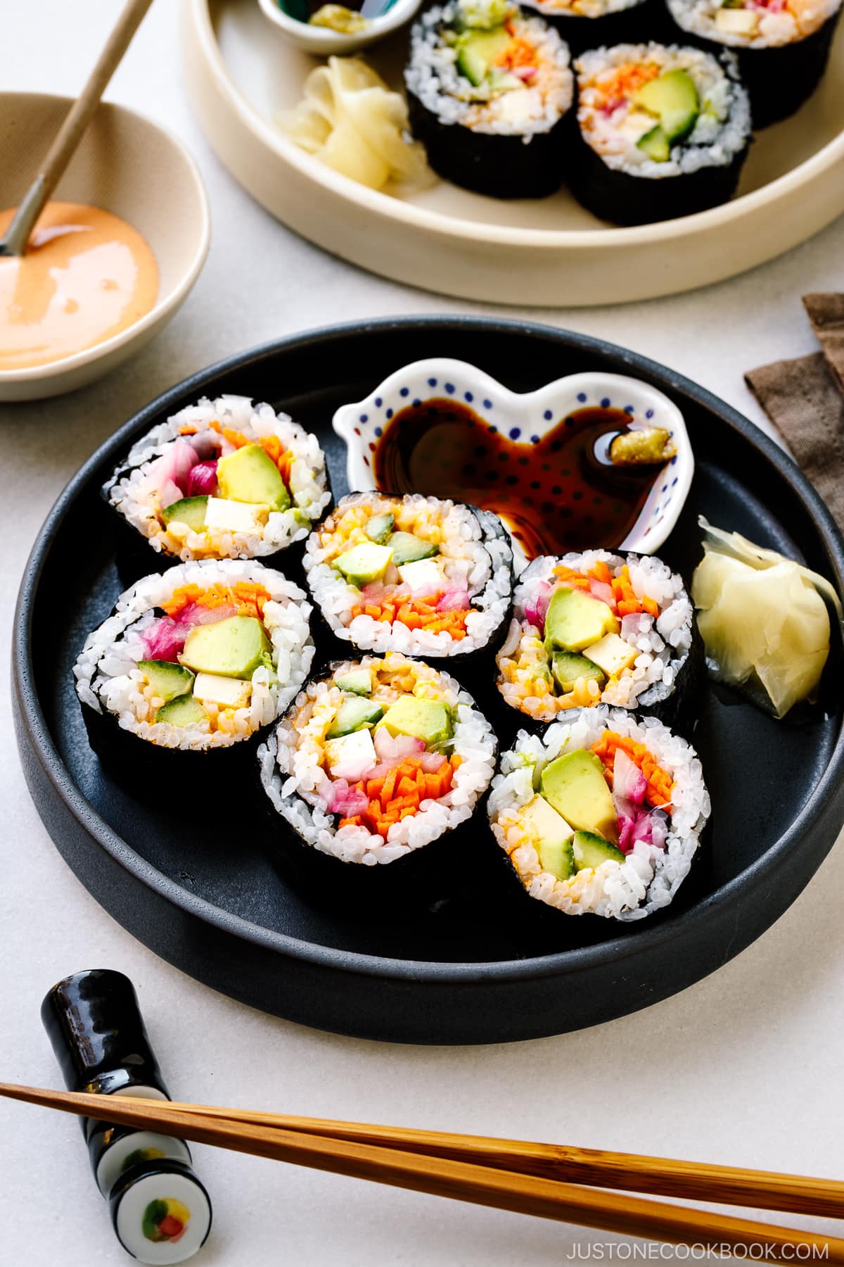 Black and white round plates containing colorful vegetarian sushi rolls.